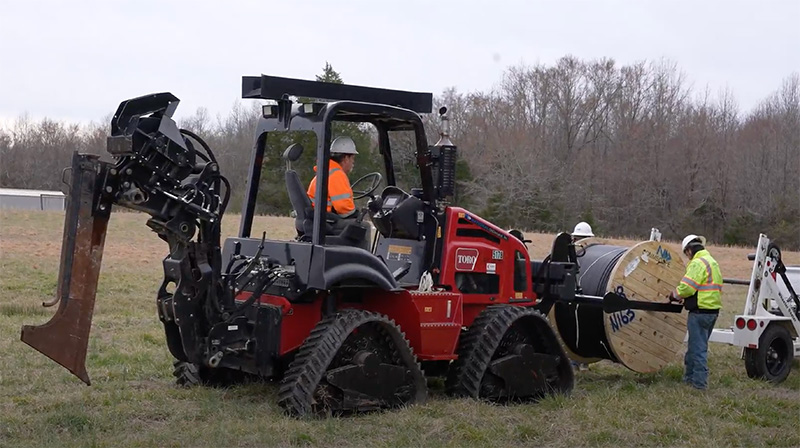 Rural Fiber Construction: 3 Aspects for Innovative Connectivity National crew adjusting a roll of fiber to prepare for a long haul plow run in rural area to support fiber construction.